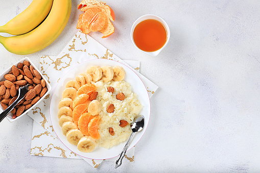 Healthy breakfast with ingredients, flat lay, rice pudding with bananas, honey, tangerines and almonds on a sunny table. Healthy and natural nutrition concept, lifestyle, nutrition for children, selective focus