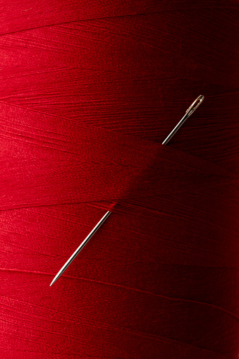 Spool of red thread with sewing needle.