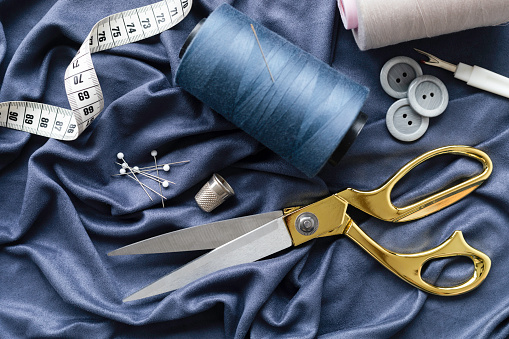 Sewing equipment like thread, needle, tape measure, scissors ,button, thimble and thread opener of blue fabric.