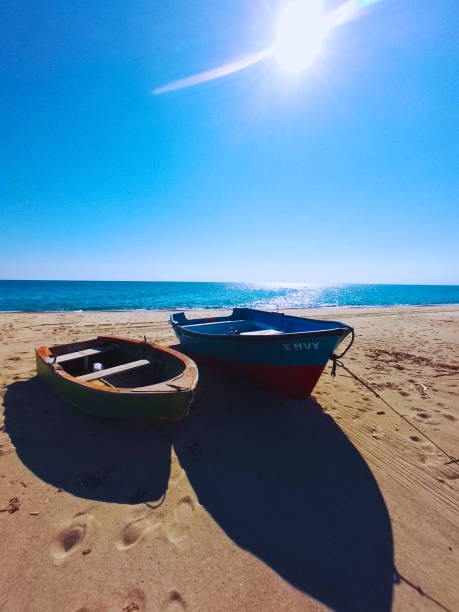 A small orange boat on a sandy beach facing a calm blue sea on a sunny summer day, symbolizing vacation, relaxation and freedom.