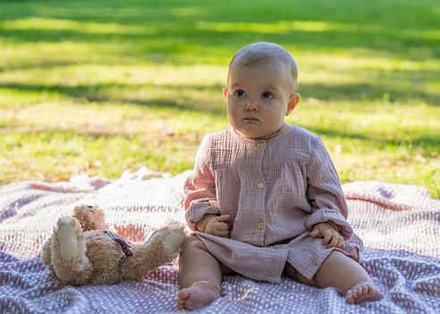 Portrait of a charming baby in a beige dress, The little girl is one year old. The child smiles. Sunny day in the park