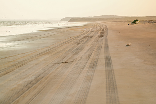 Beach at Al Khaluf with car tire tracks at sunset and small boat left on the sandy beach, Arabian sea, south of Oman.