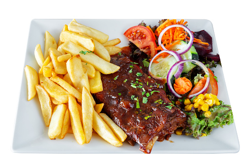 A barbecue pork dish with fresh grilled ribs, home fries and a salad with assorted vegetables. On a white insulated background. High quality photo