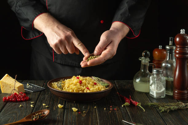 Adding aromatic spices to a bowl of pasta. The cook at the kitchen table prepares a delicious breakfast with pasta and viburnum