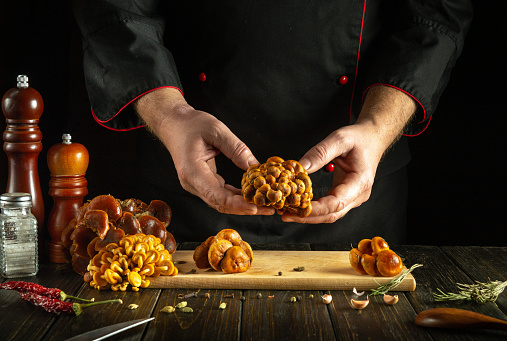 The cook prepares mushrooms in a restaurant kitchen. Chef hands sorting raw mushrooms over the kitchen table.