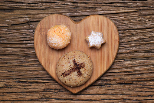 An assortment of mantecaos, alfajores, and orange crinkle biscuits on a wooden heart tray.