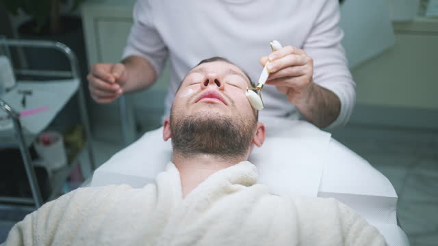 Male Therapist Using Facial Massage Roller During Skincare Treatment Of Client