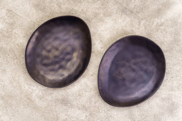 istock Pair of empty black irregularly shaped plates on concrete background above 2141679416