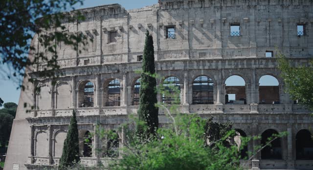 Amazing cinematic veiw of ancient Colosseum from amoung Parco Celio trees, establishment shot