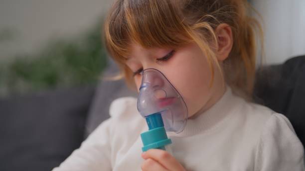 istock Small girl using nebulizer while enjoying reading book in the living room at home 2141723902