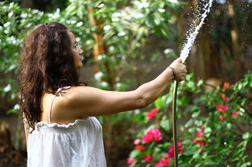 woman with long hair and white t-shirt, watering her garden