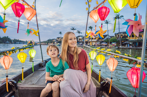 Happy family Mother and son of travelers ride a national boat on background of Hoi An ancient town, Vietnam. Vietnam opens to tourists again after quarantine Coronovirus COVID 19.
