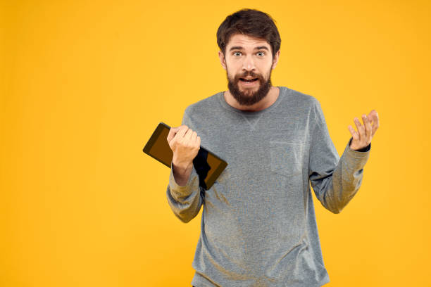 istock Emotional man with tablet in hands technology internet device lifestyle yellow background 2141826151