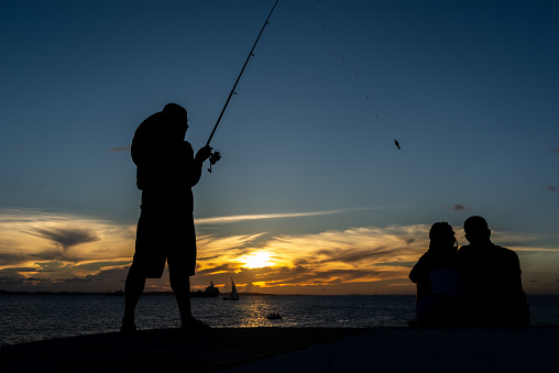 Salvador, Bahia, Brazil - April 13, 2019: Fisherman is seen in silhouette during sunset at Ponta do Humaita in the city of Salvador, Bahia.