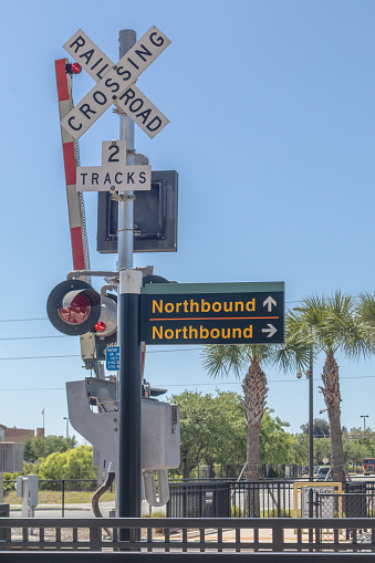 Vertical view of railroad track crossing with light, gate, northbound and southbound signs on passenger train platform