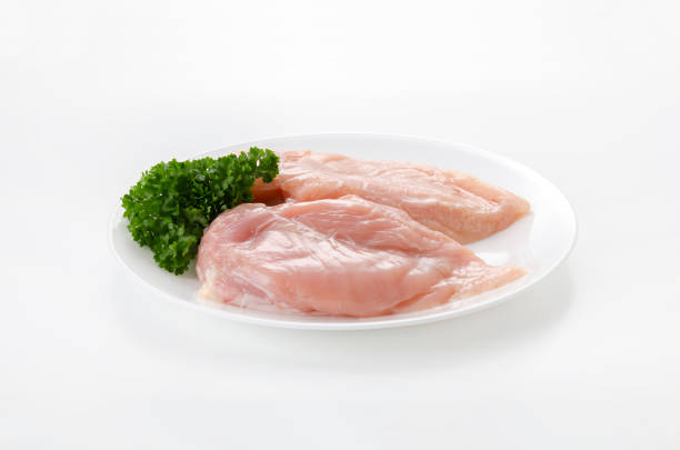 Side view close-up: chicken breast fillet with a sprig of rosemary lying on a wooden board, next to a wooden bowl with pepper seasoning and garlic on a white background. The concept of dietary dishes, a recipe for healthy and healthy food. High quality photo