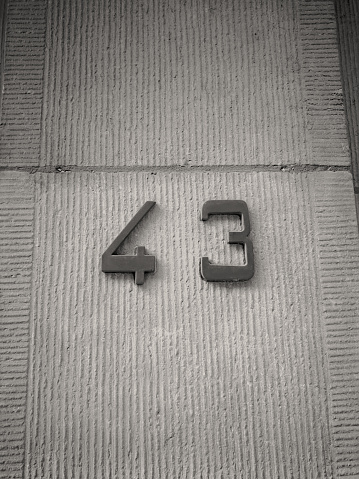 The number forty-three (43), consisting of metal applied to a textured stone surface. Black and white image. Vertical photo