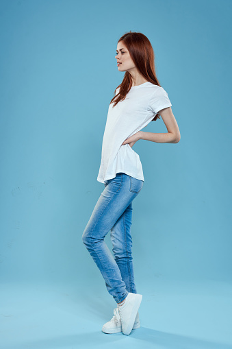 Pretty woman in white t-shirt blue jeans lifestyle in full growth studio blue background. High quality photo