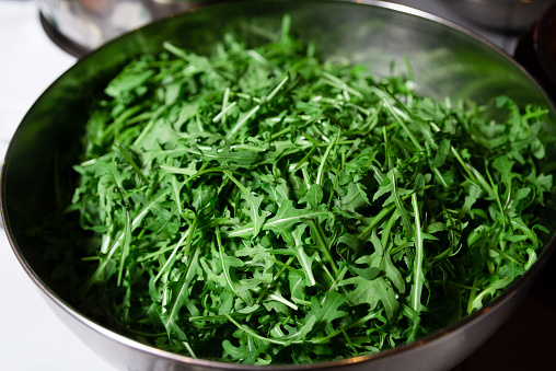 A bowl full of vibrant green arugula leaves, freshly washed and ready for salad preparation.