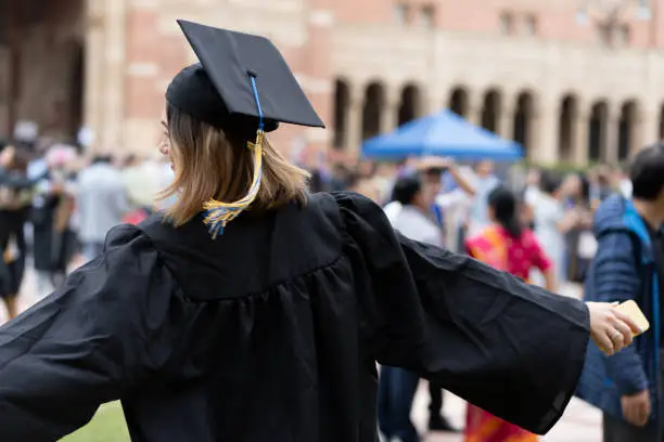 The back of a young brunette adult celebrating in front of Royce Hall, UCLA on graduation day.