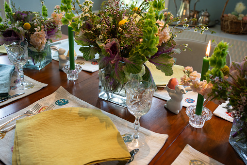 A dining table laid with colorful place settings, candles, crystal and spring flowers for Easter.