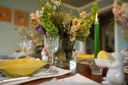 A dining table laid with colorful place settings, candles, crystal and spring flowers for Easter.