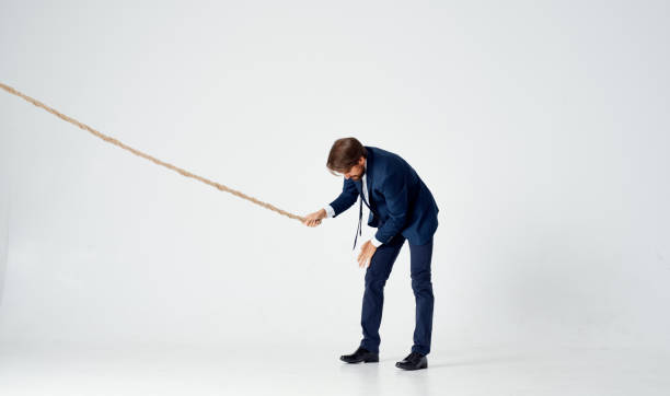 a business man lies on the floor and pulls a rope on a light background indoors. High quality photo