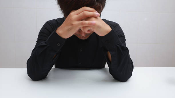 istock depressed young man sitting at the table and covering his face with his hands 2142005243