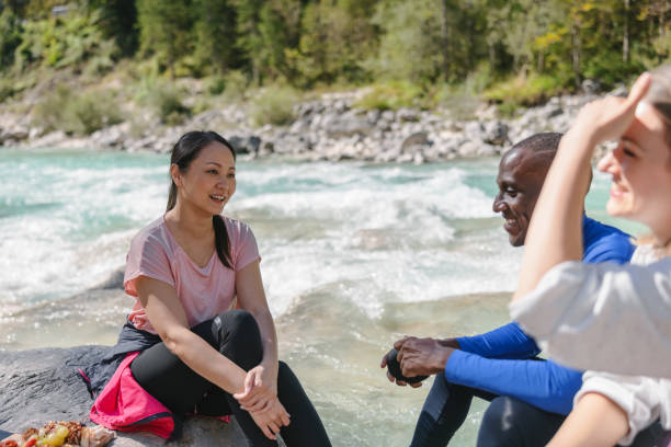 istock Three Multiracial Friends Talking While Sitting Over Some Stones Outside Next To A Turquoise River 2142012333