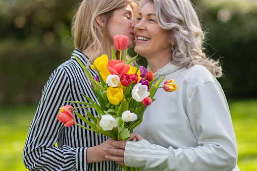 Daughter hugs mother, focus on tulip bouquet.
