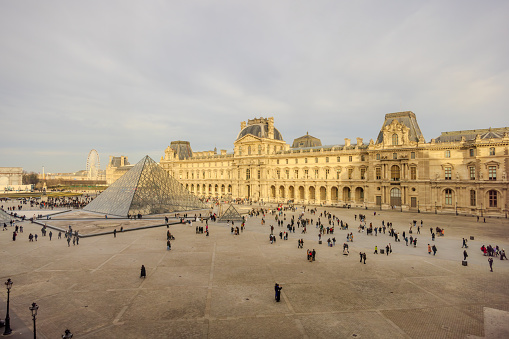 Paris, France - December 27, 2023:  Lot of tourists roaming outside Musee du Louvre with the pyramid, as viewed from an advantage point inside Musee du Louvre.  HDR encoded