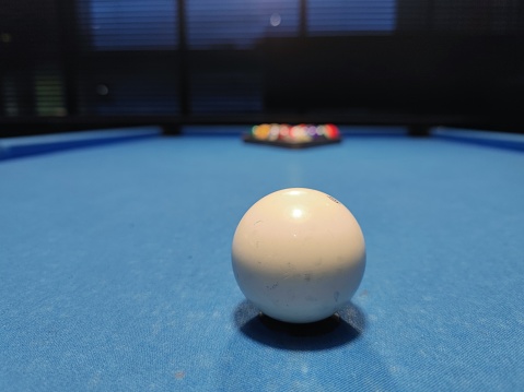 Close up shot of a white colored pool sport ball on a blue pool table at a sports bar during a tournament.  There are no recognizable persons or trademarks in the shot.