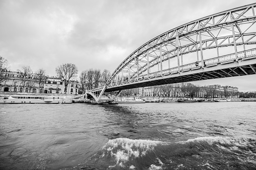 Paris, France - December 29, 2023:  Passerelle Debilly (Debilly Footbridge) over Seine River on a cloudy day, as viewed from a river cruise boat about to pass underneath it.  HDR encoded