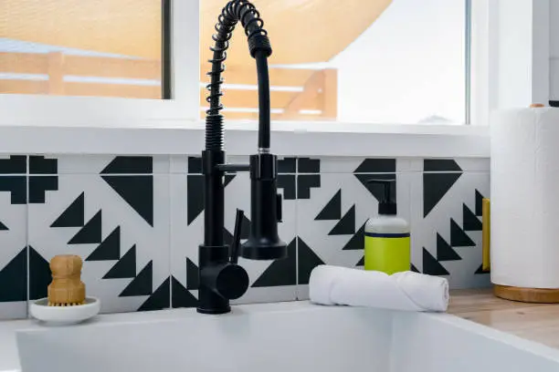 Faucet sink and soap dispenser at a kitchen window in a modern kitchen with black and white tile