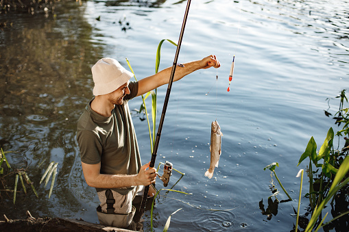 Man with fishing rod near the lake fishing at summer. Fisherman enjoying his hobby. Man wearing khaki clothes and a cap.