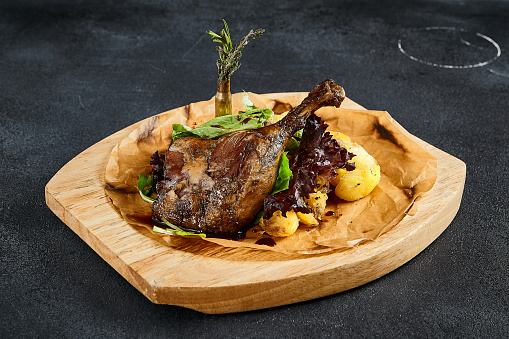 Duck leg confit with baked apples, presented on a wooden cutting board, top view. A delicious fusion of rich flavors and rustic charm.