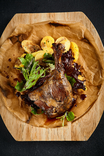 Duck leg confit with golden roasted apples, a blend of sweet and savory on a wooden presentation board, top view. Gourmet meal with a home-cooked feel.