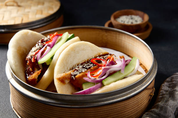 istock Authentic Asian cuisine: Bao buns with duck and vegetables in a steamer on a black table 2142295572