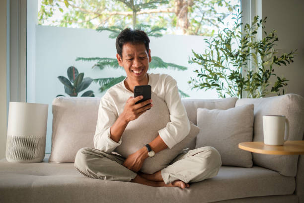 istock Happy millennial asian man typing message or ordering food delivery on smart phone while sitting in cozy home. 2142332234