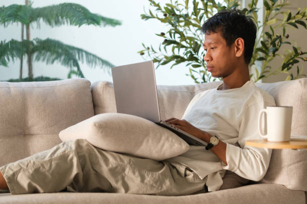 istock Smiling millennial man using laptop while sitting on comfortable sofa at home. 2142332747