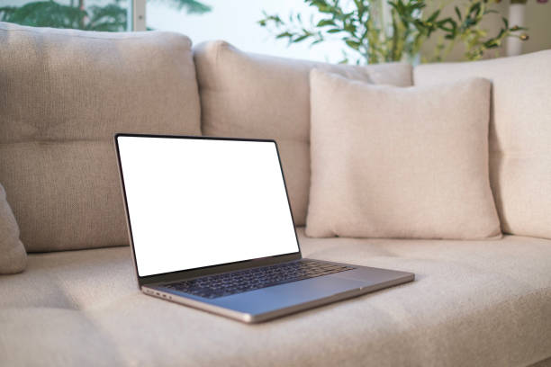 istock Laptop computer with blank screen on couch sofa with pillows. Aesthetic elegant styled home living room interior design template with mockup copy space. Online store, blog, social media, shop branding 2142332756