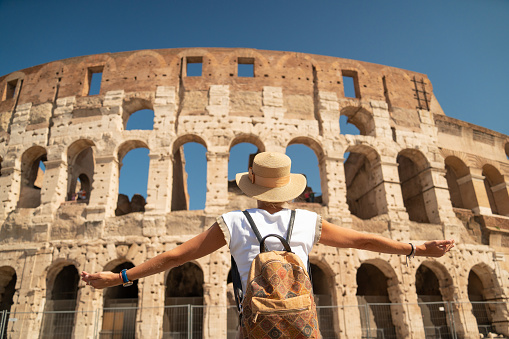 Woman tourist with arms outstretched in front of the Colosseum in Rome, a famous landmark of the eternal city, capital of Italy