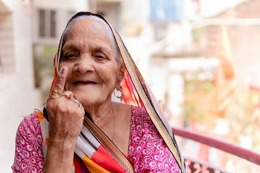 Portrait of happy Indian senior woman in sari showing ink-marked finger after voting for the election and looking at the camera with a smile.