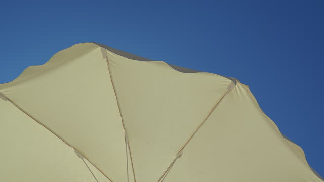 White beach umbrella. Blue sky in the background. View from below. Relaxing context. Summer holidays by the sea. General contest and location