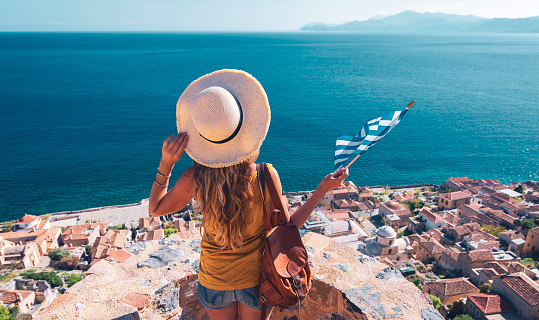 Travel destination in Greece-Traveler woman with bag, hat and Greek flag-Road trip, Adventure, summer vacation concept