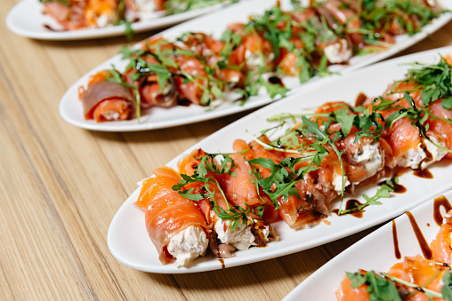 Delectable smoked salmon roll-ups filled with cream cheese and garnished with arugula, presented on white platters for a catered event.