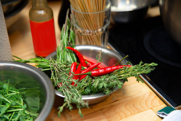A chef's kitchen setup featuring a bowl of fresh herbs and red chili peppers, with cooking utensils in the background.