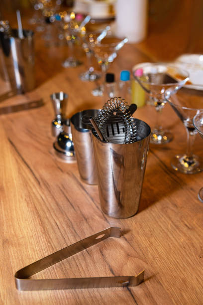 An array of professional mixology tools including shakers, strainers, and a bar spoon, artfully arranged on a polished wooden surface.