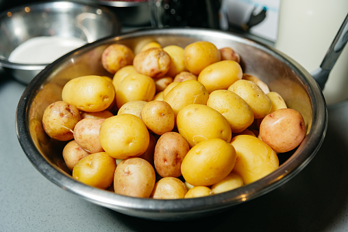 A stainless steel bowl filled with clean, whole raw potatoes on a kitchen counter, indicating preparation for a meal.