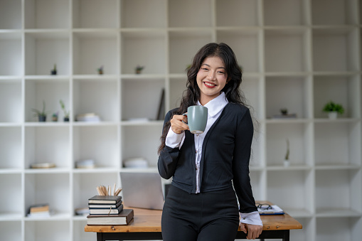 Freelance Asian woman standing relaxing holding a hot drink while taking a break.
